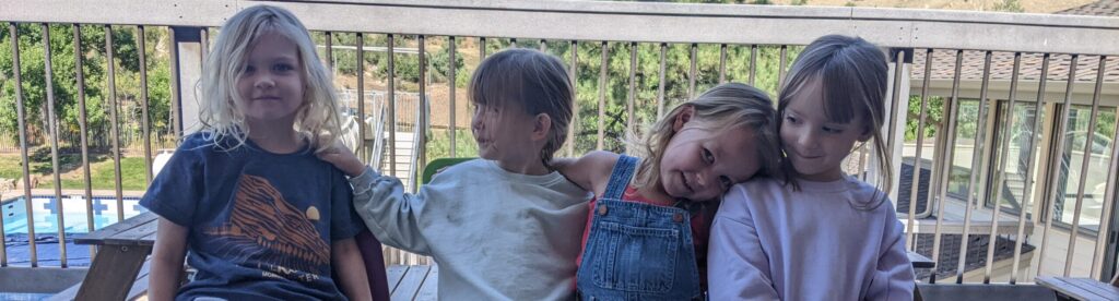 four preschool students sitting in on chairs outside on a patio