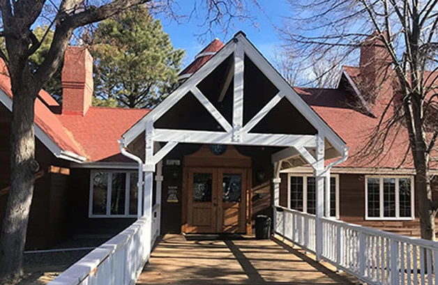 Front entrance of a rustic lodge-style building with a red roof, wooden siding, and a ramp leading to double doors.